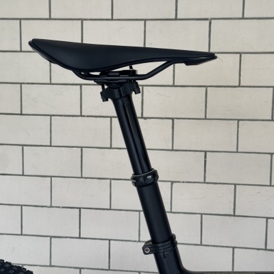Assento de bicicleta preto sobre estrutura preta com texto ADVANCED DYNAMICS e parede branca de azulejos ao fundo
