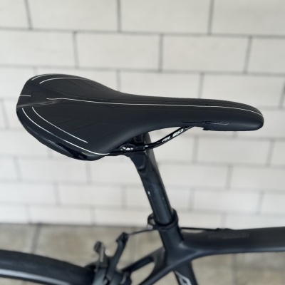 Sela preta com riscas brancas numa bicicleta preta, com parede branca de azulejos ao fundo