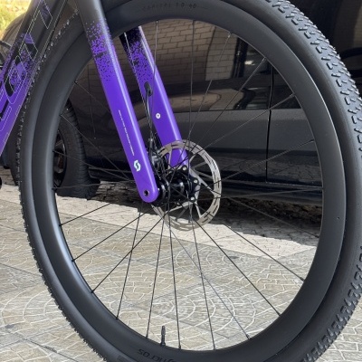 Roda dianteira de bicicleta com garfo roxo e pneu preto Schwalbe G-One RX.