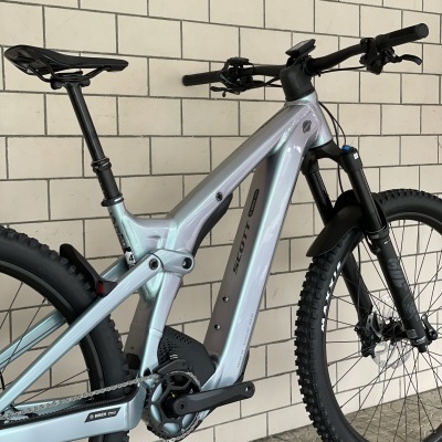 Bicicleta elétrica de montanha prateada encostada numa parede de azulejos brancos