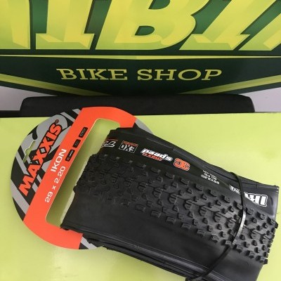 Pneu de bicicleta Maxxis Ikon 29 x 2.20 preto com embalagem laranja e cinzenta sobre superfície verde clara