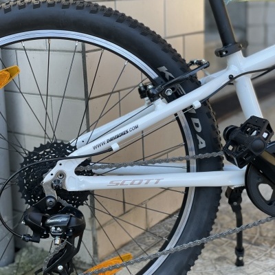 Roda traseira de bicicleta branca Scott com pneus pretos e fundo de parede clara e chão de azulejos.