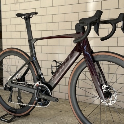 Bicicleta de estrada de carbono em roxo escuro e preto contra parede de tijolos claros