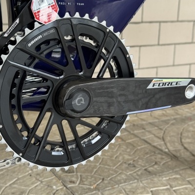 Pedaleira e prato preto de bicicleta SRAM Force com estrutura azul escuro e piso de pedra ao fundo