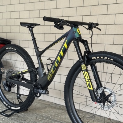 Bicicleta de montanha Scott preta e verde com letras amarelas junto a parede de tijolos brancos