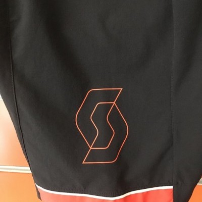 Peça de roupa preta com detalhe vermelho e logótipo geométrico vermelho