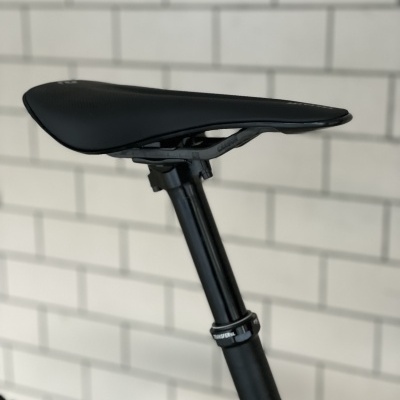 Selim de bicicleta preto com canote ajustável contra parede de azulejos brancos