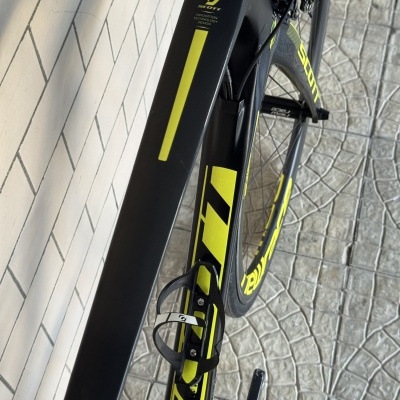 Bicicleta de estrada preta e amarela da marca SCOTT colocada junto a uma parede de azulejos brancos