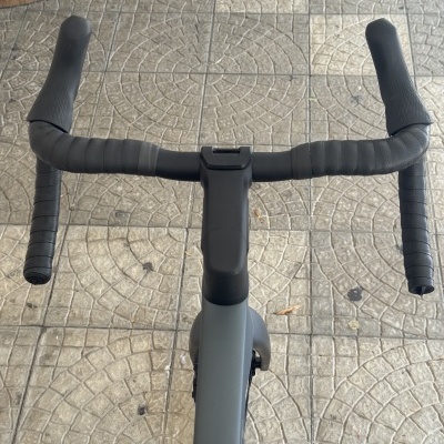 Guidão preto de bicicleta de estrada com fita preta, visto de cima sobre chão de pedra com padrão geométrico.