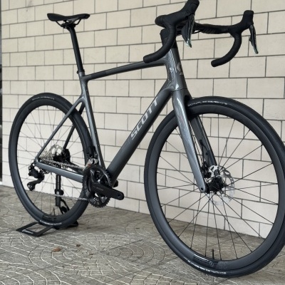 Bicicleta de estrada cinza SCOTT com pneus Schwalbe ONE encostada a parede de azulejos