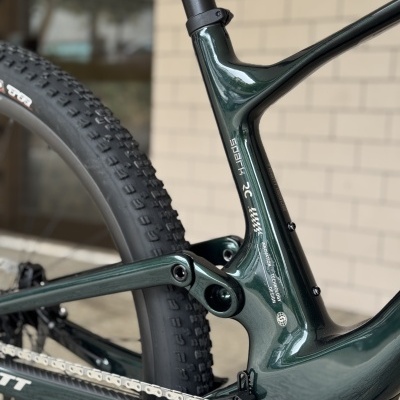Frame de bicicleta de montanha em carbono verde escuro com texto branco e pneus pretos com relevo