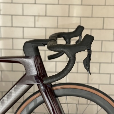 Bicicleta de estrada com quadro vinho e cinza, guiador preto, pneus com flanco bege