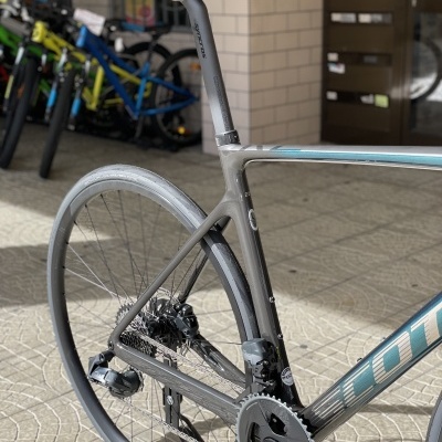 Bicicleta de estrada cinza com selim preto e fundo com várias bicicletas e parede azulejada