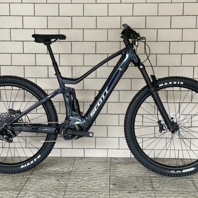 Bicicleta eléctrica de montanha Scott preta junto a uma parede de azulejos brancos