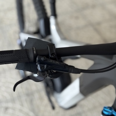 Guiador de bicicleta com punho e manete de travão preto, quadro cinzento e branco ao fundo