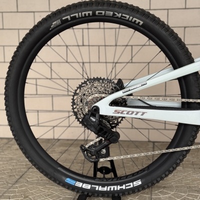 Roda traseira de bicicleta com pneus pretos, quadro branco SCOTT e sistema de mudanças Shimano.