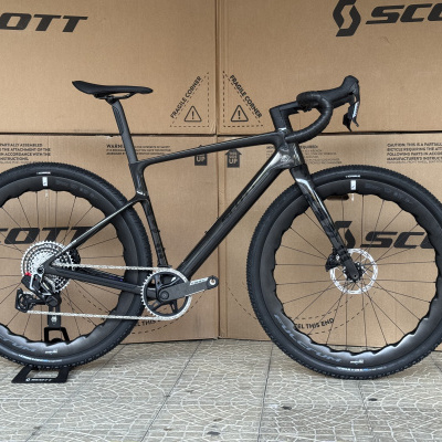 Bicicleta Scott preta com pneus Schwalbe e aro de carbono Fulcrum em frente a caixa de cartão Scott