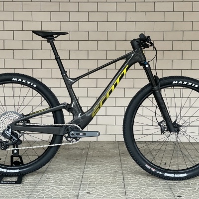 Bicicleta de montanha cinzento escuro com logo amarelo Scott e pneus Maxxis pretos