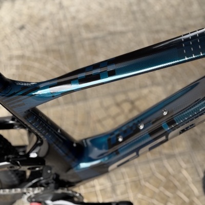 Quado bicicleta carbono azul metálico com padrão geométrico preto sobre calçada clara