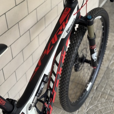 Bicicleta de montanha preta, branca e vermelha com texto SCOTT e DANI.BIKES num ambiente interior