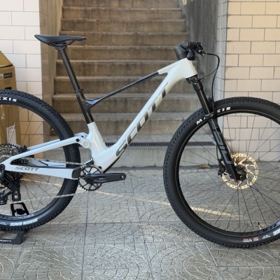 Bicicleta de montanha branca e preta com pneus MAXXIS e suspensão, apoio num suporte