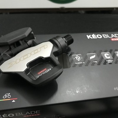 Pedal automático preto e branco KÉO BLADE CARBON sobre caixa preta do produto