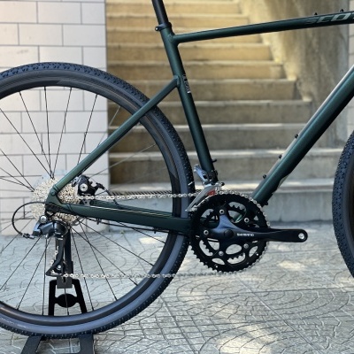 Bicicleta verde escuro com pneus pretos e componentes Shimano em fundo urbano