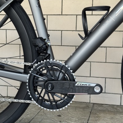 Bicicleta de estrada cinzenta com componentes SRAM FORCE junto a parede de azulejos brancos