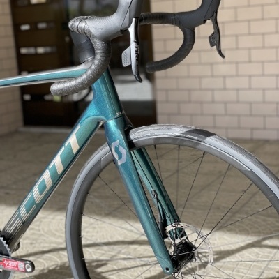 Bicicleta de estrada azul metálico com letras SCOTT e guiador cinza em ambiente urbano