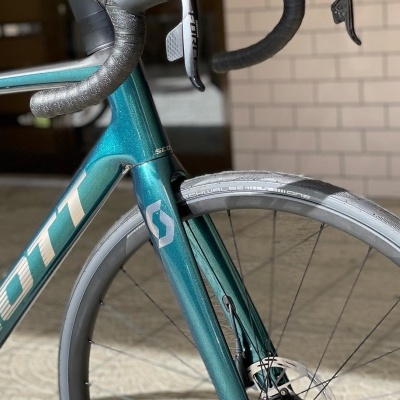 Bicicleta de estrada azul metálico com guiador curvo e pneus pretos junto a parede de tijolos