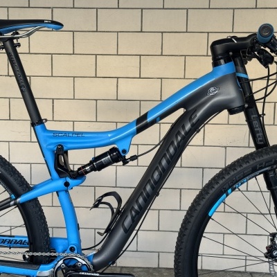 Bicicleta de montanha azul e preta Cannondale Scalpel junto a um muro de azulejos bege