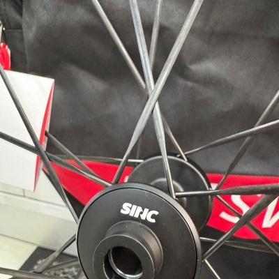 Roda de bicicleta com raios metálicos e eixo preto com texto JNC