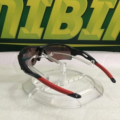 Óculos desportivos com armação preta e hastes vermelhas sobre suporte transparente