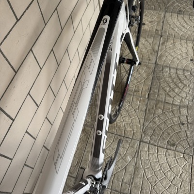 Bicicleta de estrada SCOTT branca e preta junto a uma parede de azulejos brancos.