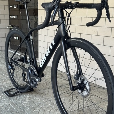 Bicicleta de estrada de carbono preta com detalhes brancos e pneus CONTINENTAL perto de uma parede de azulejos.