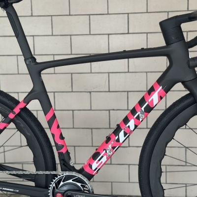Bicicleta de estrada preta e rosa com logotipo SCOTT contra parede de azulejos brancos