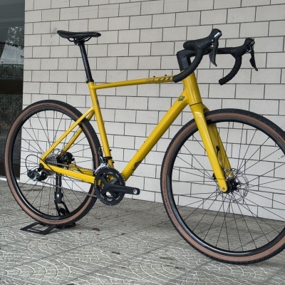 Bicicleta de corrida amarela com guiador e selim pretos encostada a parede branca de azulejos.