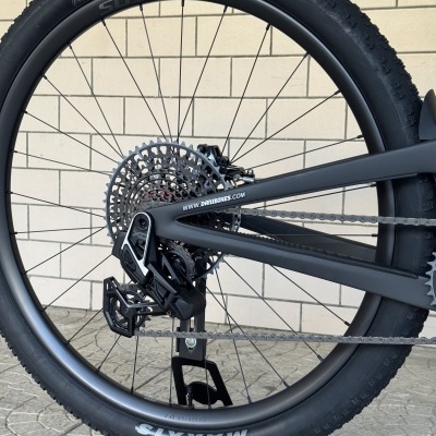Roda traseira de bicicleta com pneu preto, aro preto, corrente e desviador, fundo com parede e chão de pedra