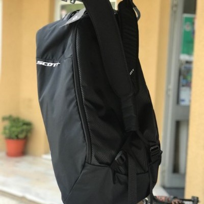 Mochila preta SCOTT pendurada com alças acolchoadas e bicicleta ao fundo