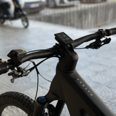 Guiador de bicicleta preta com display digital e manípulos, em ambiente urbano com chão de lajetas