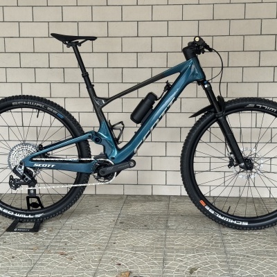 Bicicleta de montanha azul e preta SCOTT com pneus Schwalbe e suspensão, em parede branca