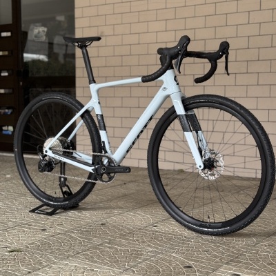 Bicicleta de estrada branca e preta com pneus grossos apoiada numa superfície pavimentada