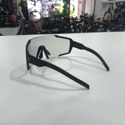 Óculos desportivos pretos com lentes claras sobre mesa branca numa loja de bicicletas.