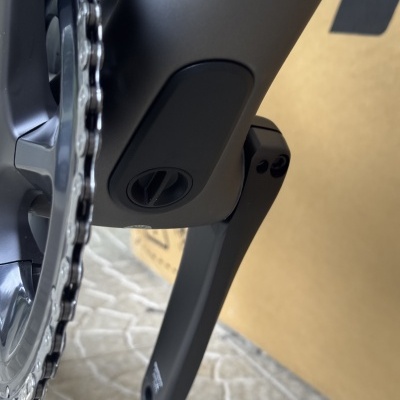 Pedaleira e corrente de bicicleta preta fosca com fundo de chão e caixa de cartão.