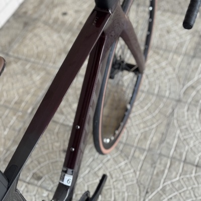 Bicicleta de corrida com quadro bordô e pneus com bordas castanhas sobre piso de azulejos cinzentos