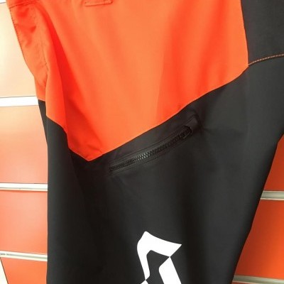 Calças desportivas laranja e preto com bolso e logótipo branco penduradas num cabide