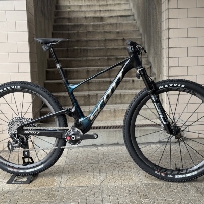 Bicicleta de montanha preta SCOTT encostada numa estrutura metálica com escadas ao fundo