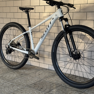Bicicleta de montanha branca com pneus pretos e componentes em preto encostada numa parede de azulejos brancos