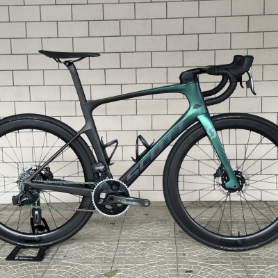 Bicicleta de estrada preta e verde metálico com quadro de carbono e rodas aerodinâmicas