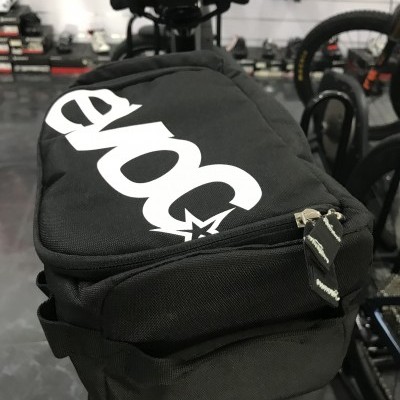 Bolsa preta de bicicleta com logótipo branco evoc num ambiente de loja de bicicletas.